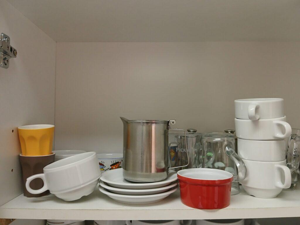 A cupboard filled without structure with various types of cups, containers and bowls.