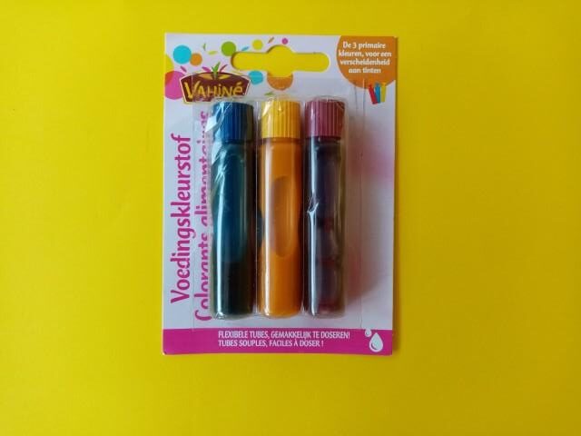 Three bottles of food colorant inside of their packaging. The colors are blue, yellow and red